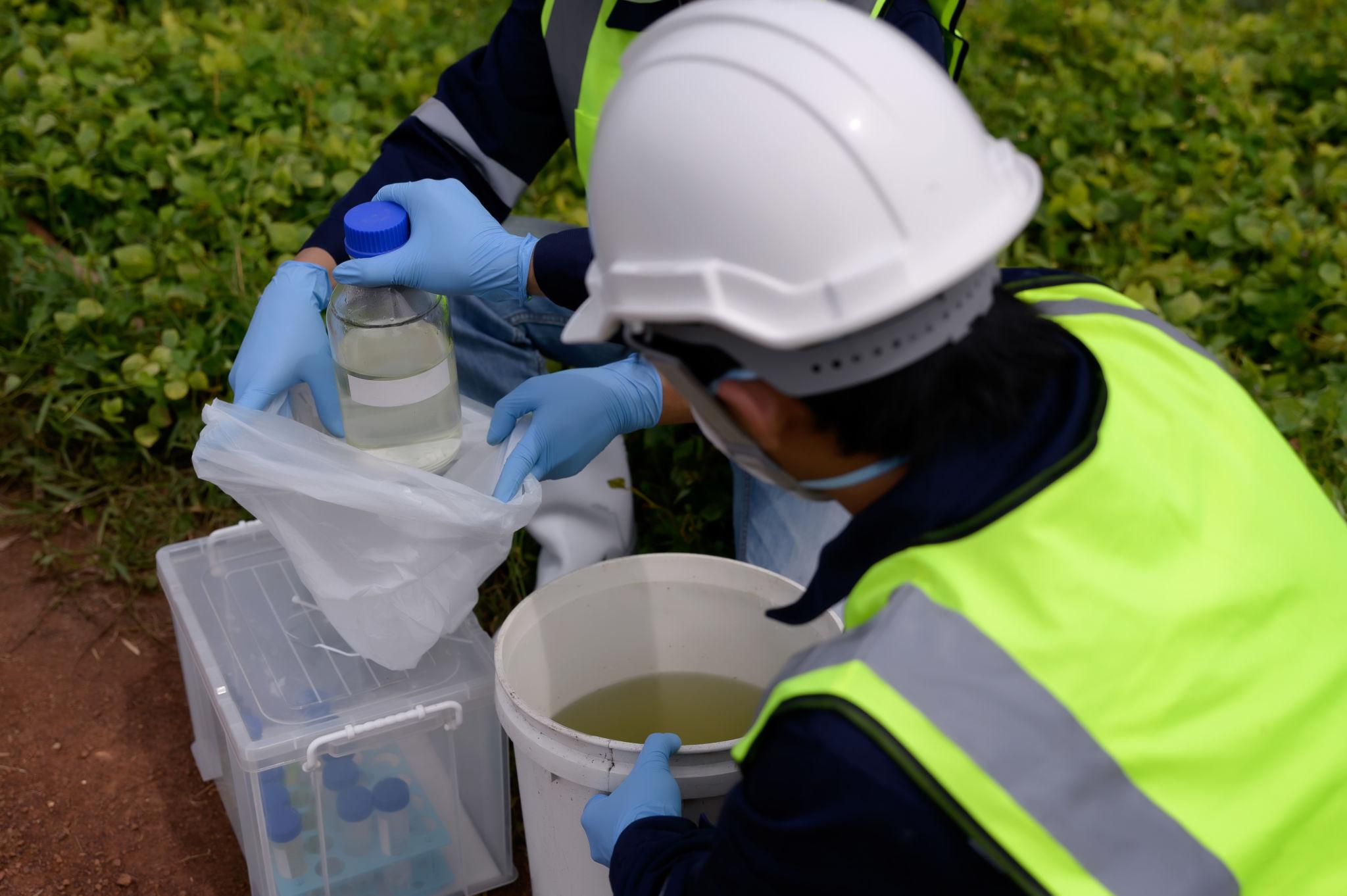 Environmental technician collecting a water sample using protective equipment for water quality testing